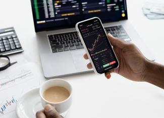 A person holding a smartphone. On the phone screen is a series of charts and graphs showing an investment's performance.